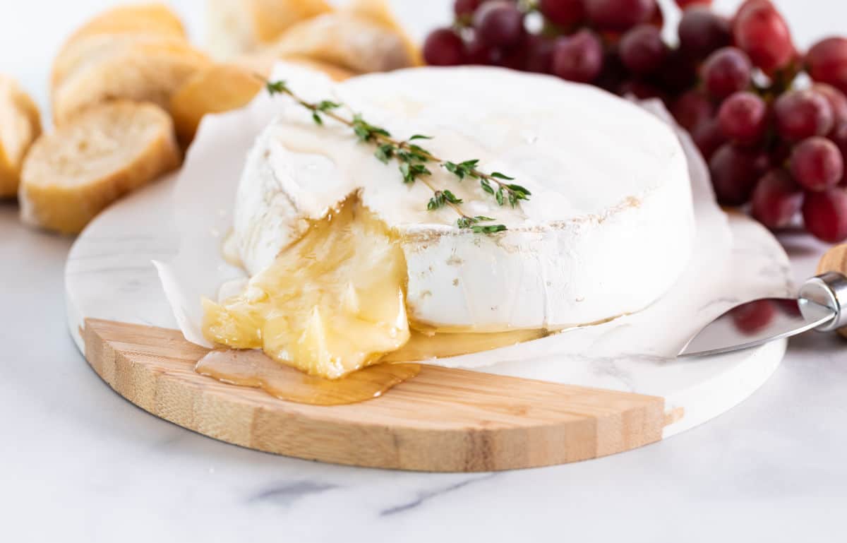 Melted Brie on wood board with thyme, grapes, and bread.
