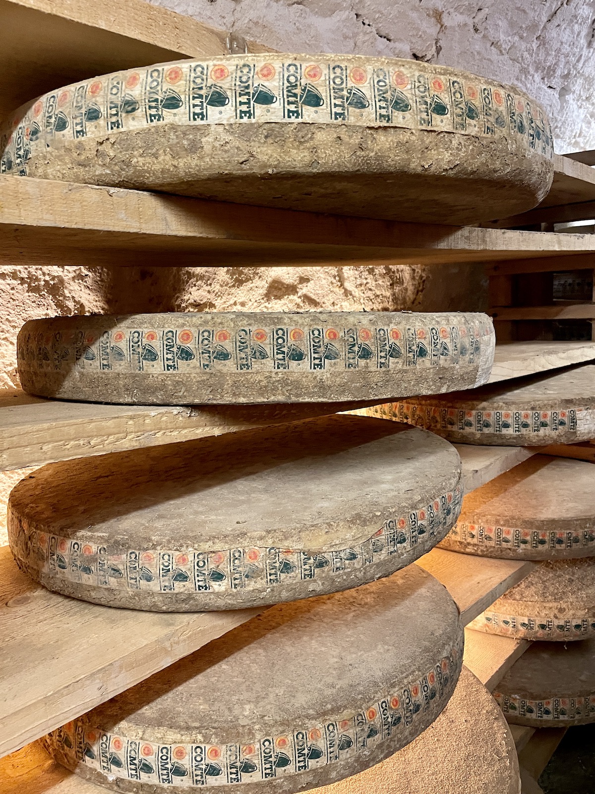Wheels of Comte Cheese on wood shelves.