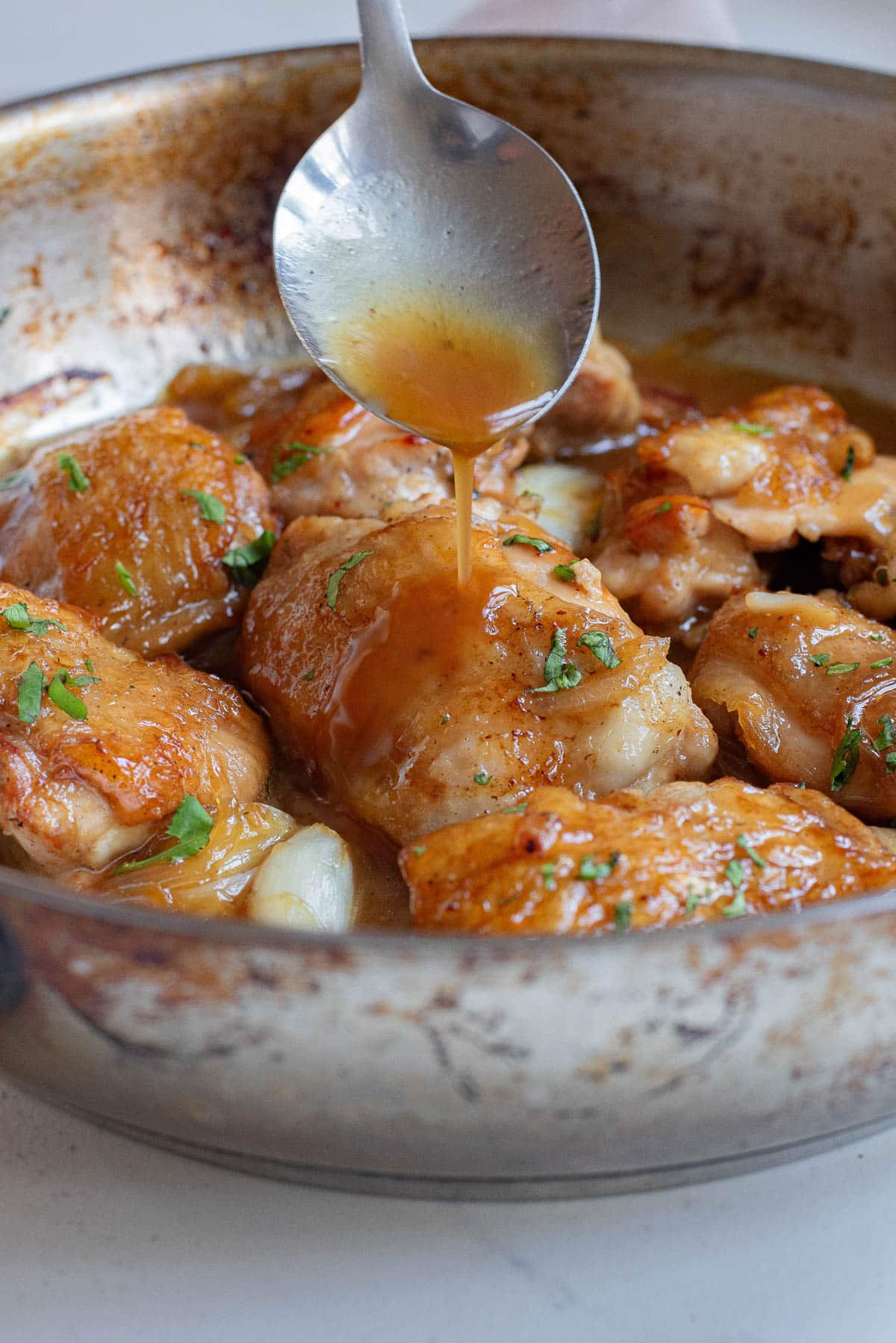 Spooning gravy over cooked chicken thighs in a skillet.