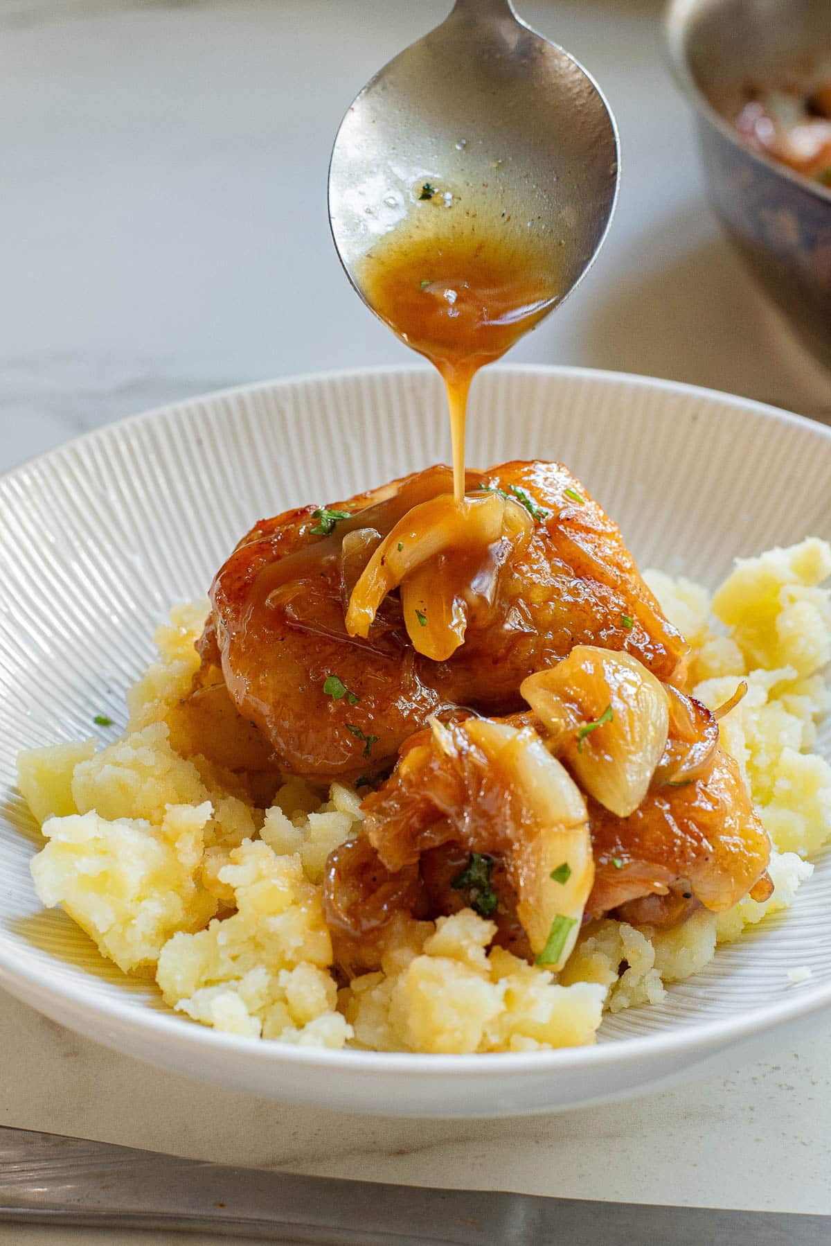 Chicken thigh over mashed potatoes with spoon dripping gravy over dish.