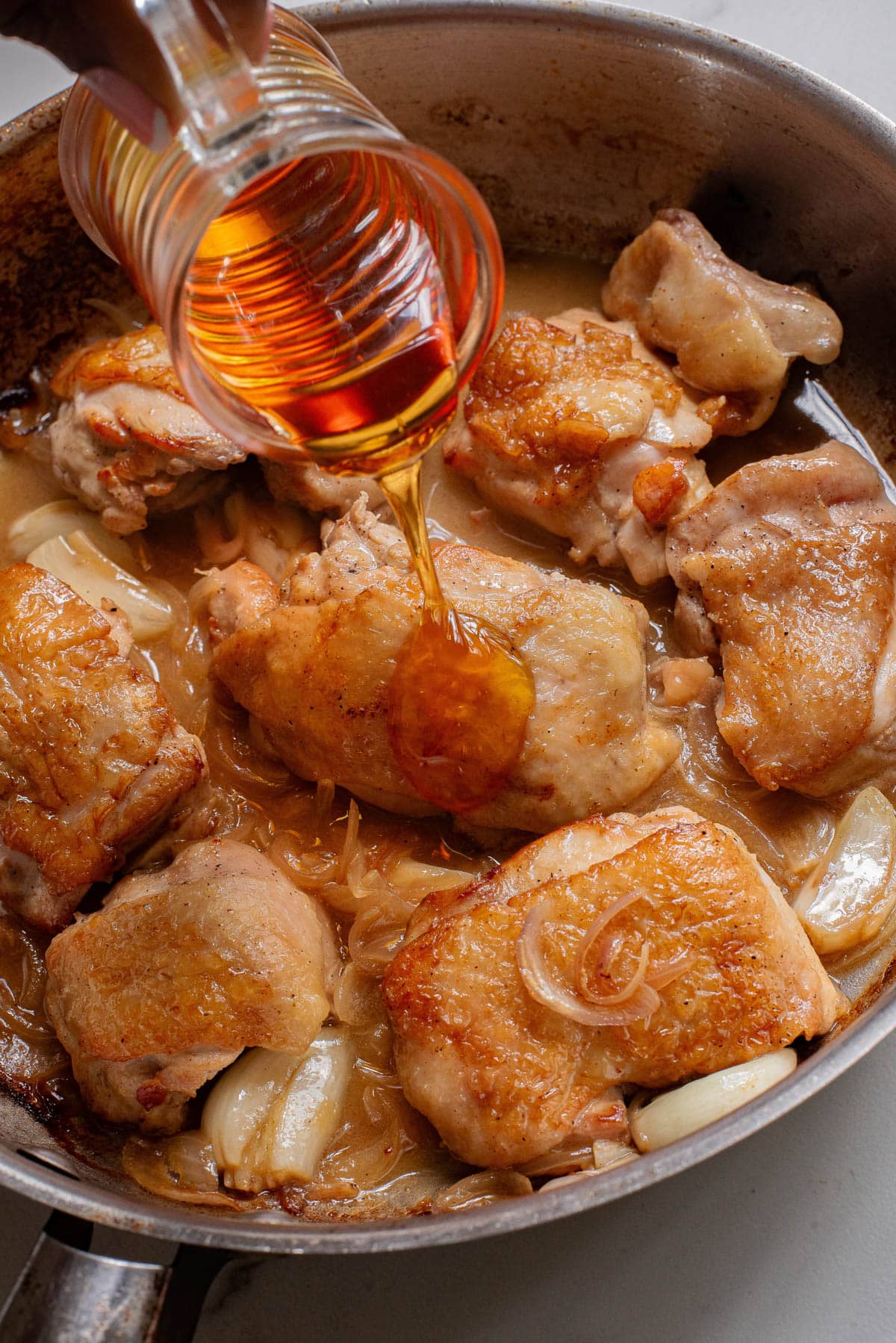 Pouring honey over cooked chicken thighs in a skillet.