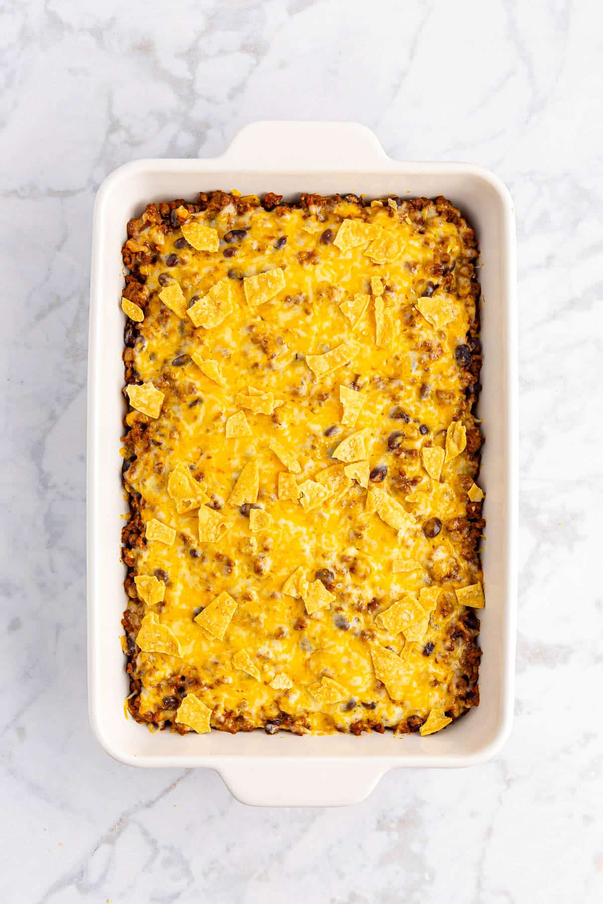 Taco casserole beef with cheese and taco chips in white casserole dish.
