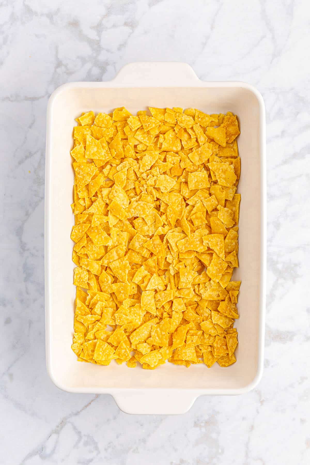 Crushed tortilla chips in white casserole dish.