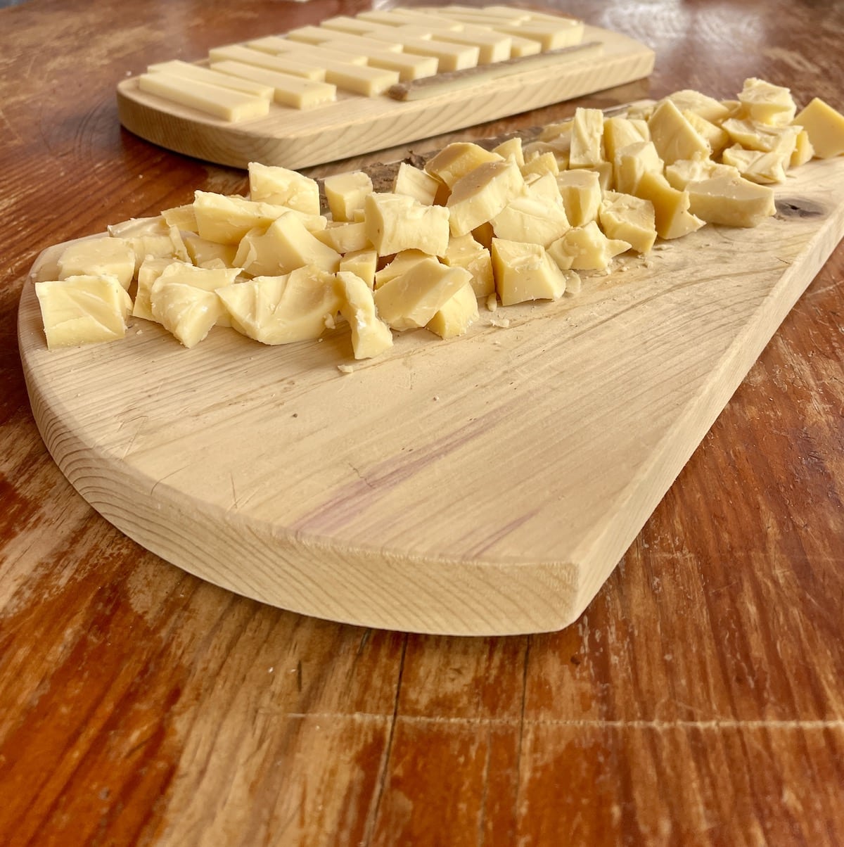 Aged Comte cheese on a wood cutting board on a wood table.