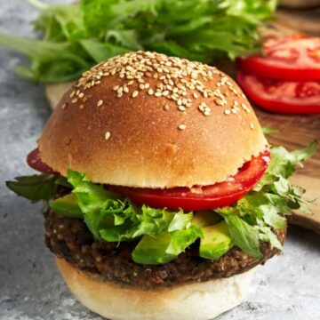 Black bean burger with lettuce, tomato, and avocado on a sesame seed bun.