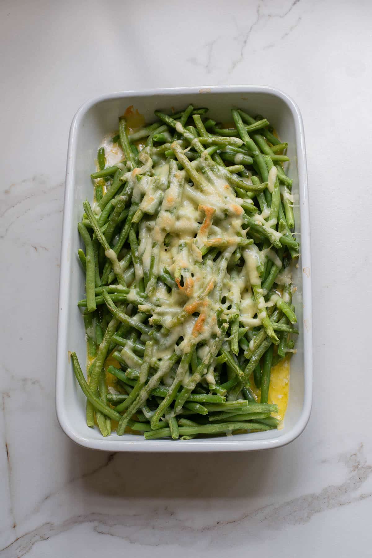 Green beans in white baking dish with melted cheese.