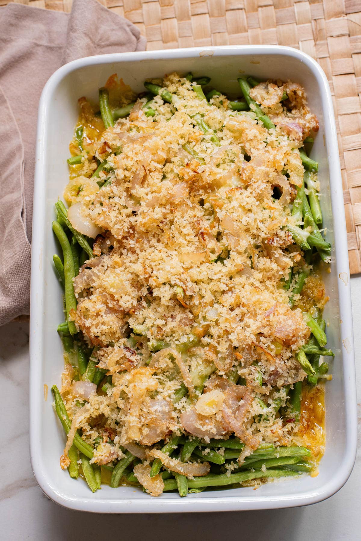 Broiled Green bean casserole in white baking dish with crispy onion topping.