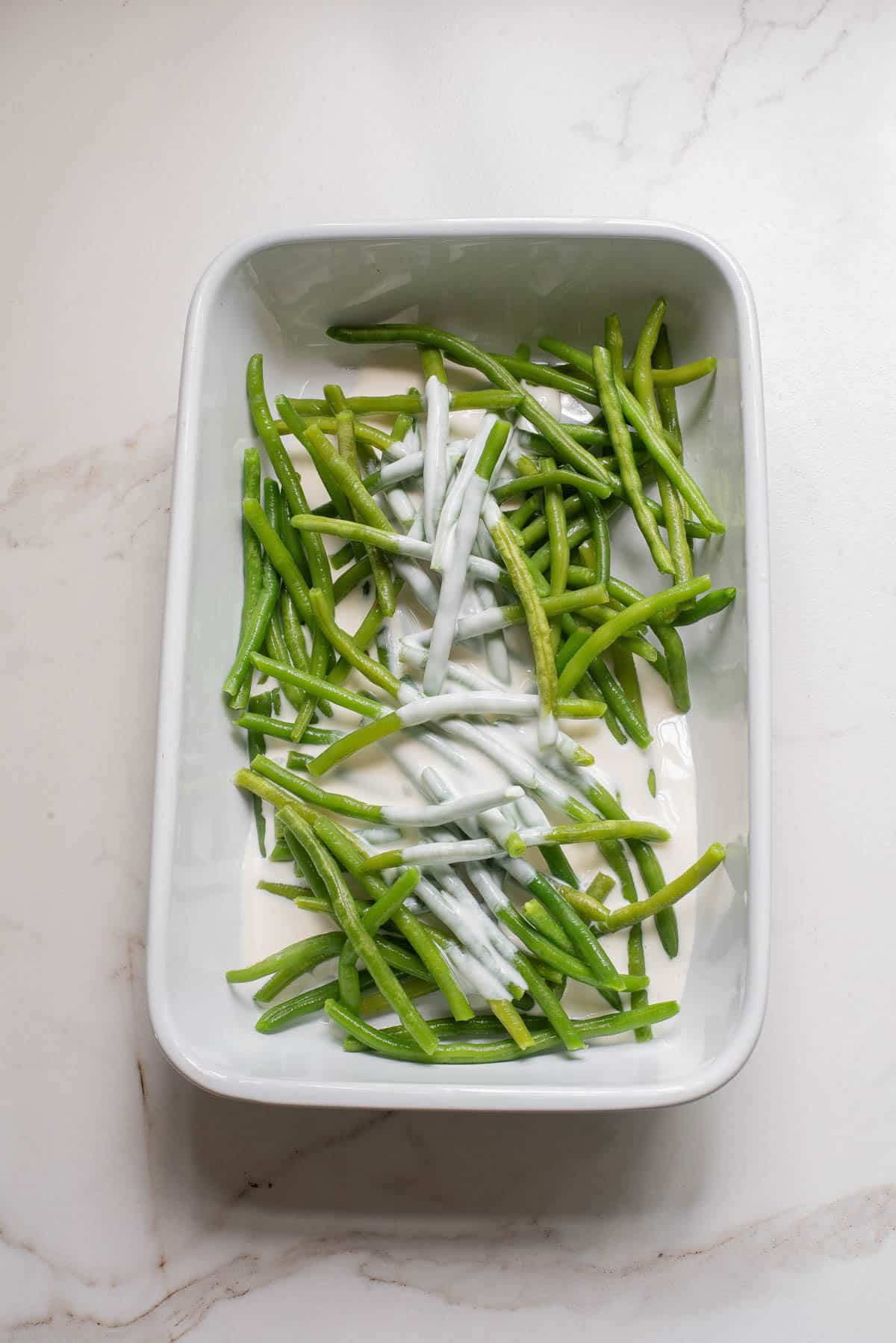 Green beans in white baking dish with heavy cream.
