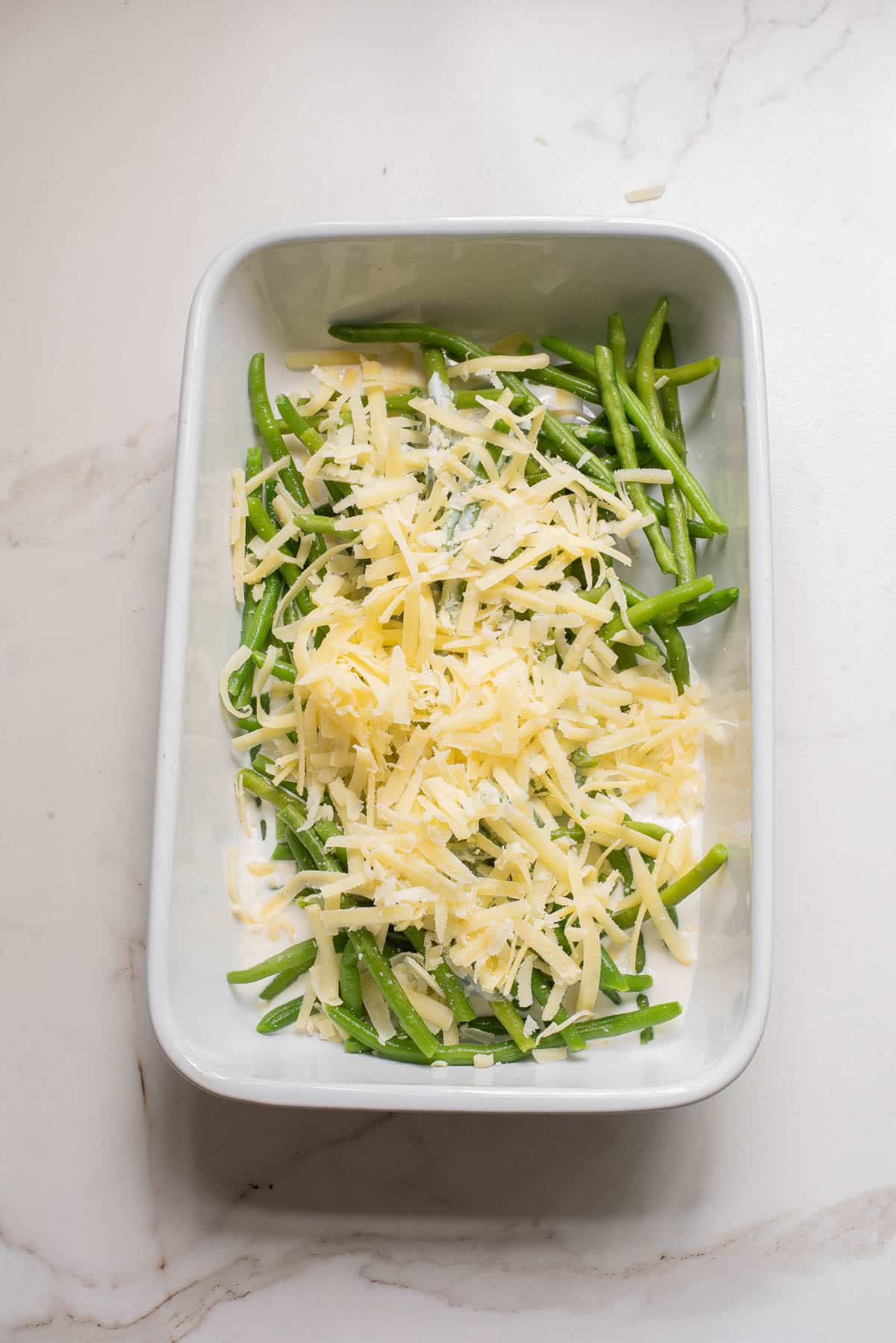 Green beans in white baking dish with cream and cheeses.