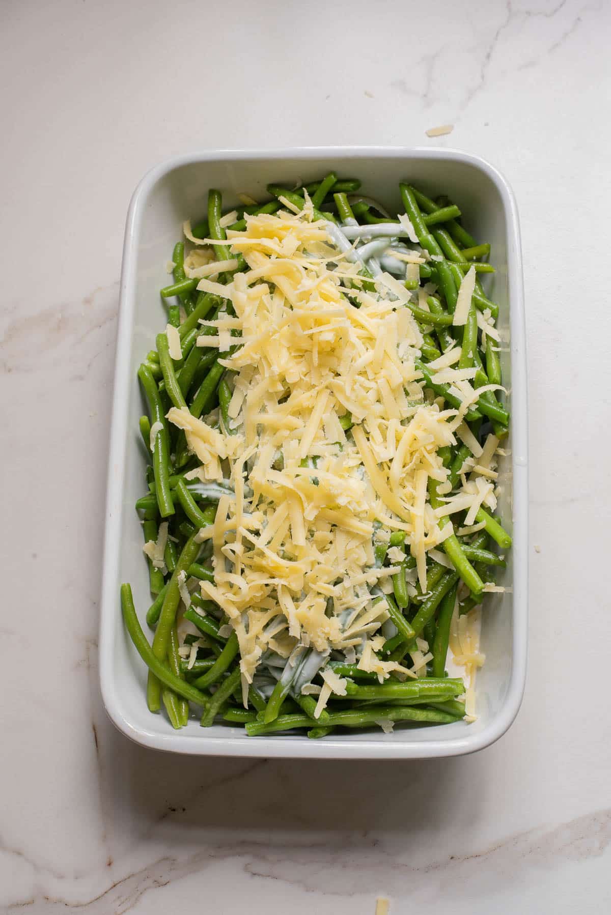 Green beans in white baking dish with cream and cheeses.