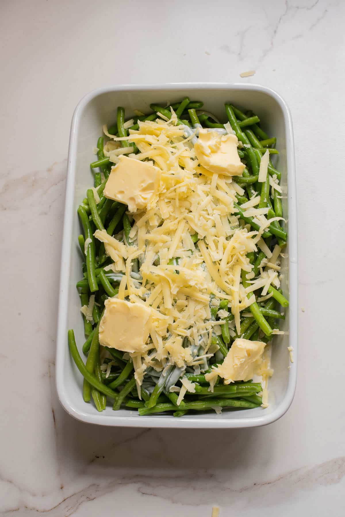 Green beans in white baking dish with cream, cheeses, and butter.
