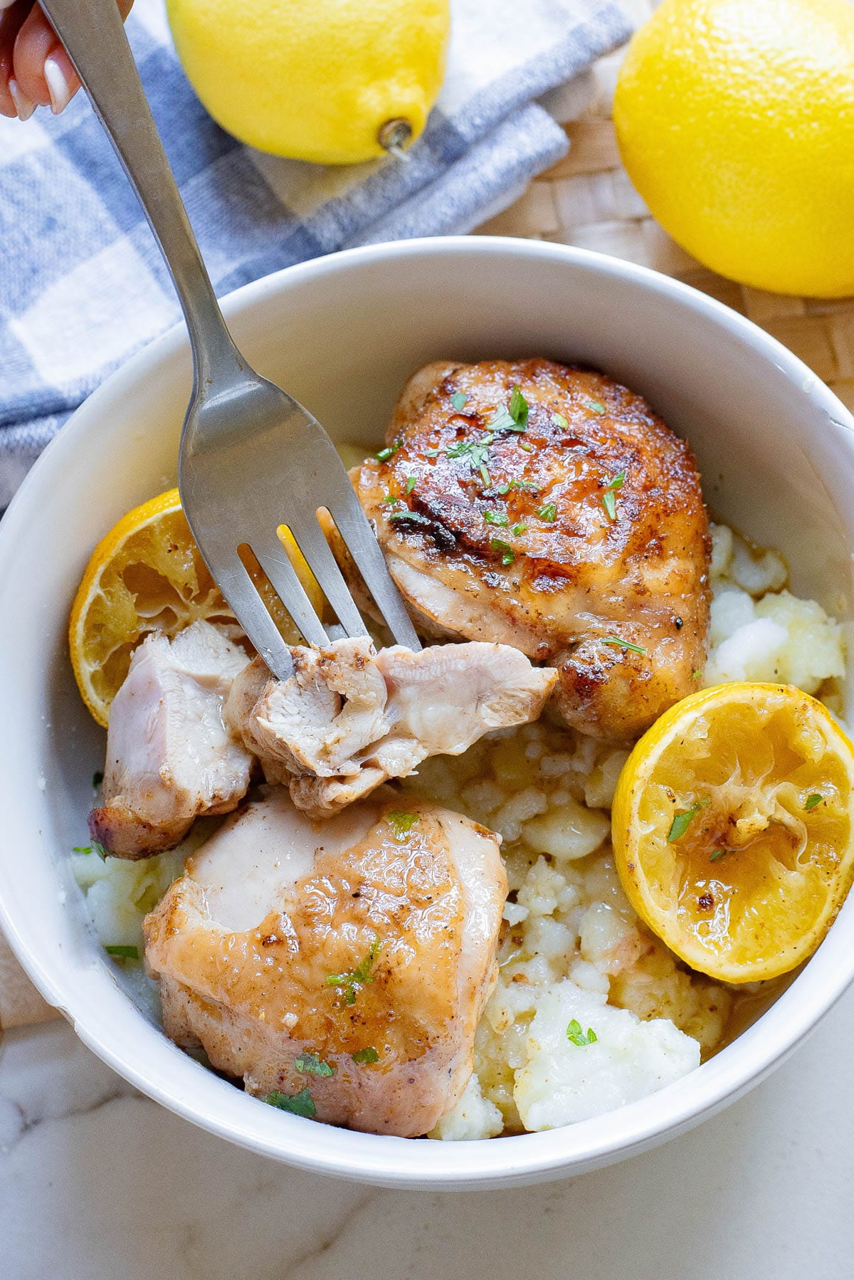 Chicken thighs in a white bowl with rice and piece on fork with lemon on side.