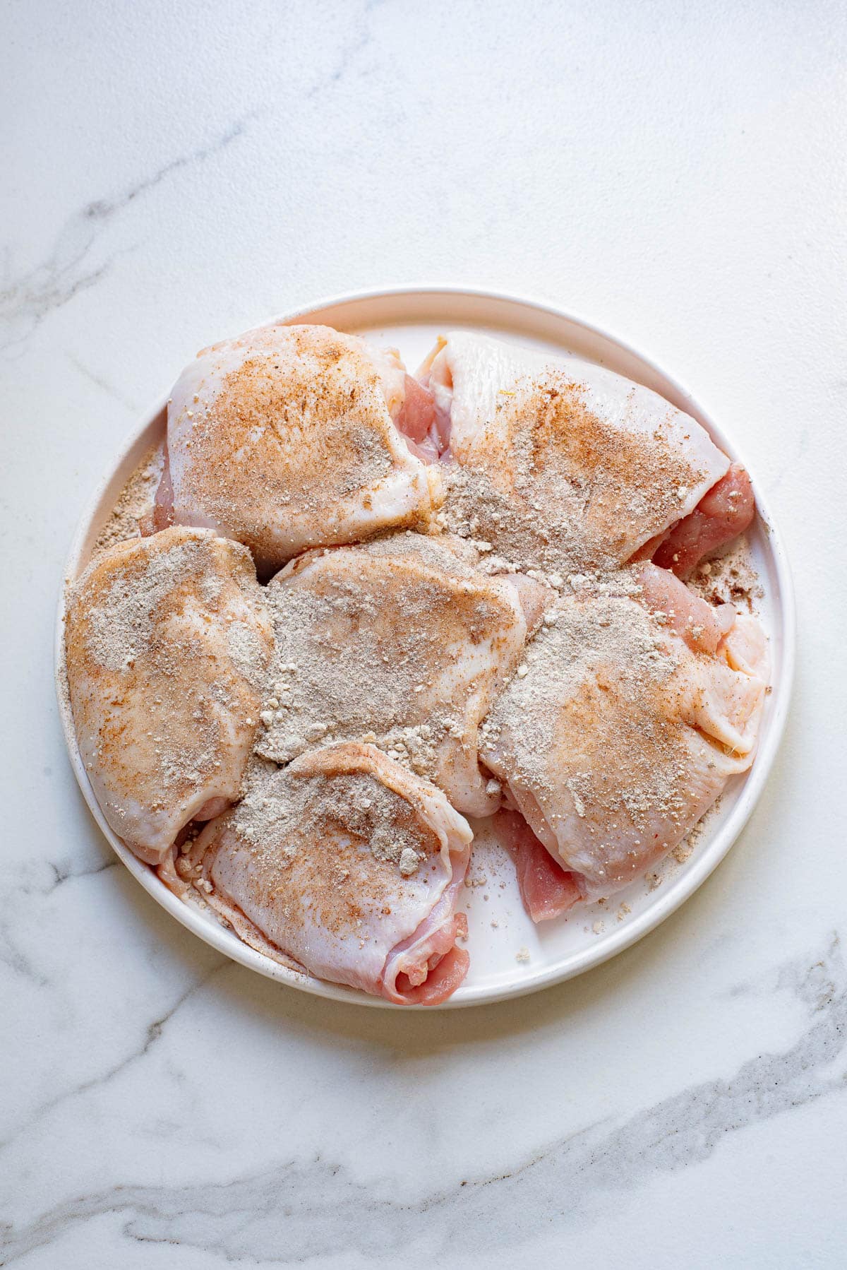 Raw chicken with seasoning in a white bowl.