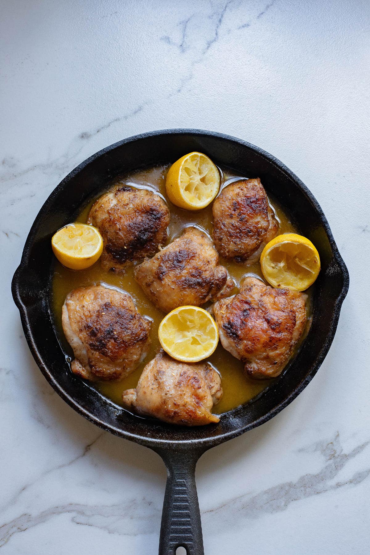 Chicken seared in a cast iron pan with juices and lemons.