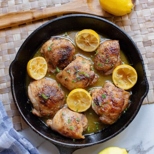Chicken thighs in lemon sauce with lemons on side in case iron skillet.