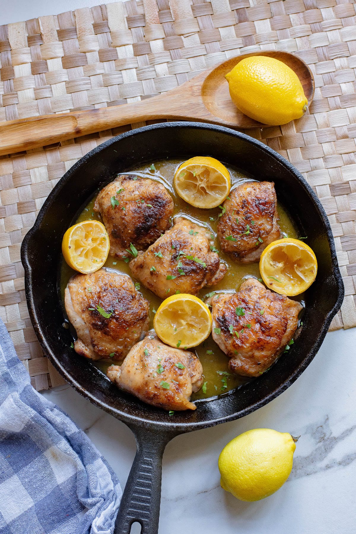 Chicken thighs in lemon sauce in cast iron pan with lemons and herbs.
