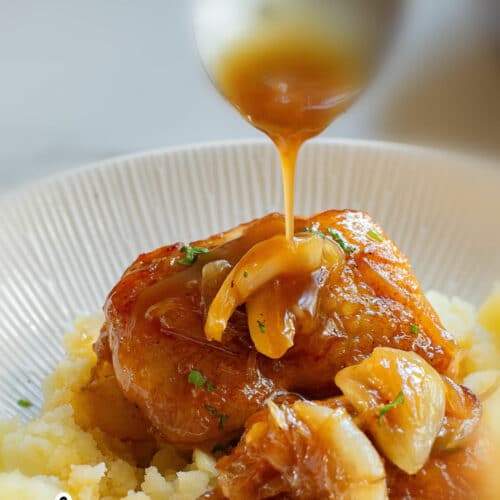 Chicken thighs over mashed potatoes with spoon dripping gravy over dish.