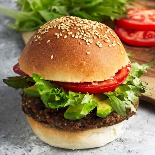 Black bean burger with lettuce, tomato, and avocado on a sesame seed bun.