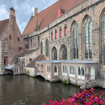 Historic building on a canal with flowers on railing of bridge.