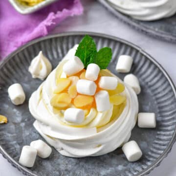 Pavlova recipe on a grey plate with marshmallows and fruit.