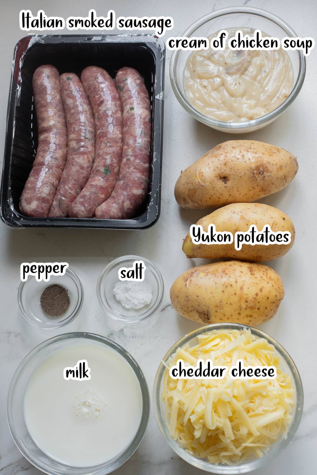 Sausages, soup, potatoes, salt, pepper, cheese, and milk on a marble counter.
