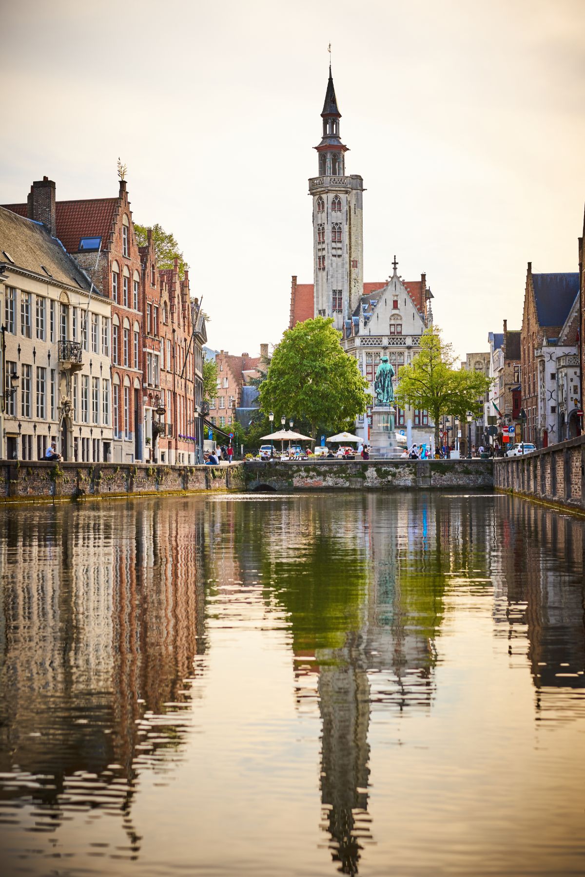 Jan van Eyck statue and historic buildings at the end of a canal in Bruges.