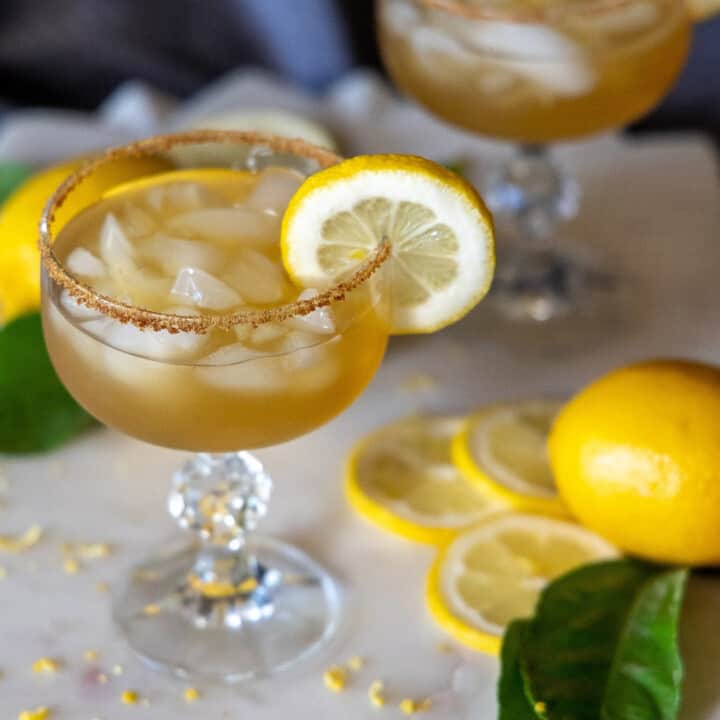 Lemon cocktail in a martini glass with a lemon wheel on the side.
