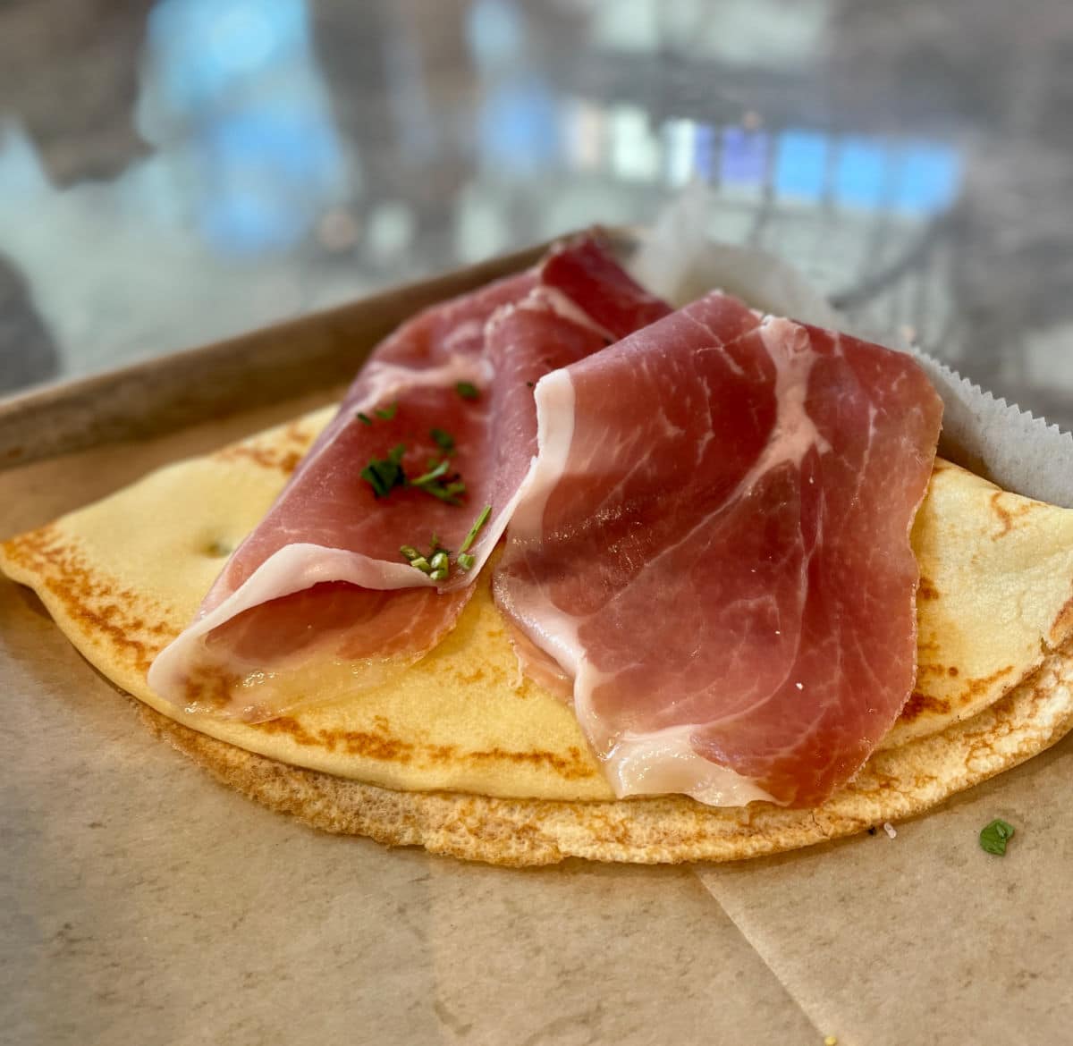 Crepe with cheese and prosciutto on a tray.