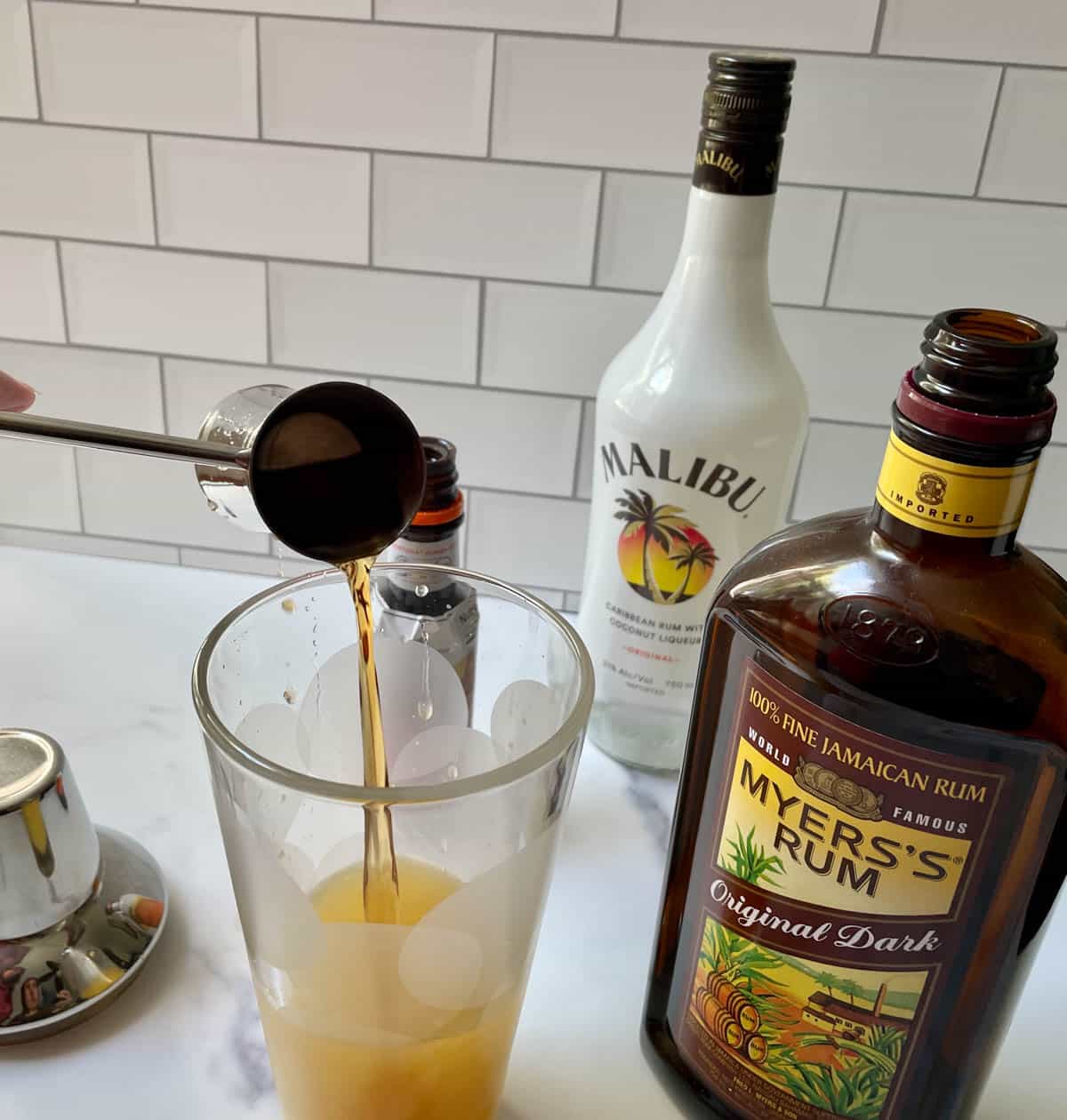 Adding darm rum to bitters and juice in a cocktail shaker. 