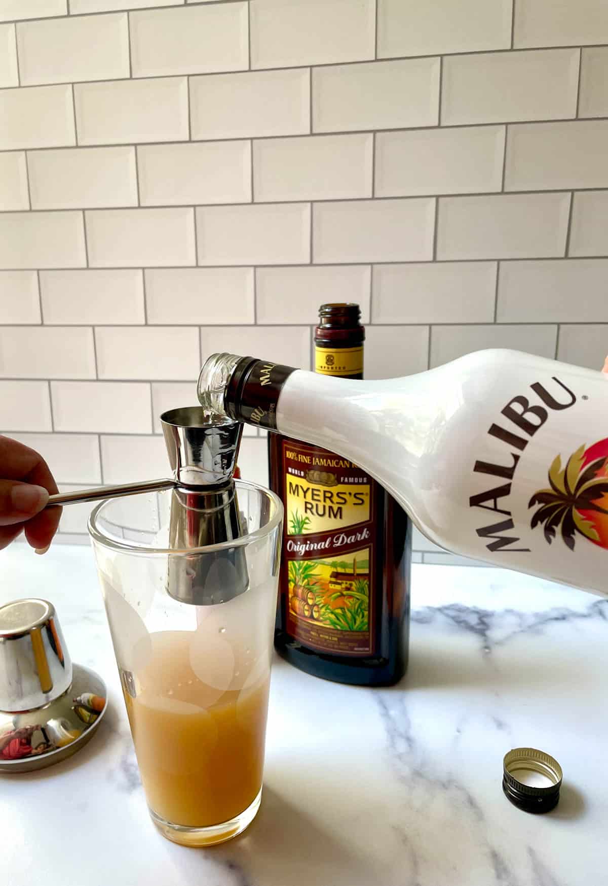 Adding rum to bitters and juice in a cocktail shaker. 