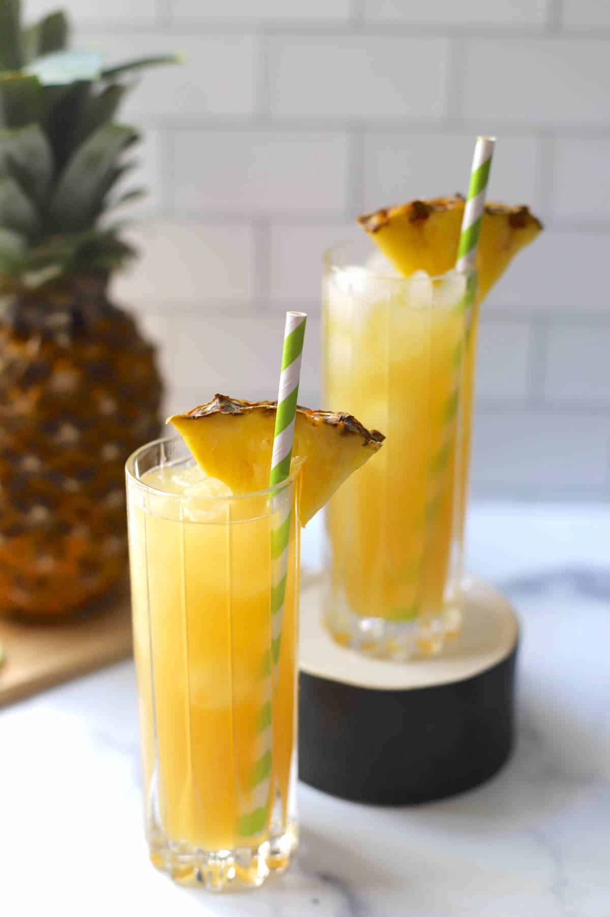 Yellow cocktail in a tall glass with pineapple wedge and straw.