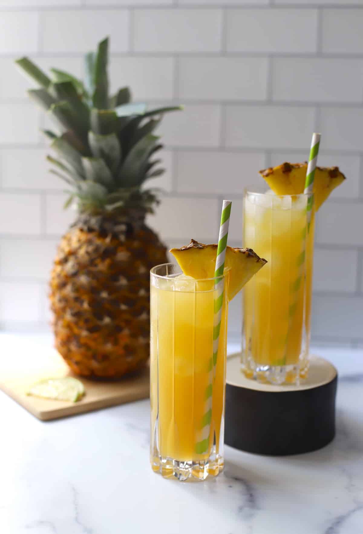 Yellow cocktail in a tall glass with pineapple wedge and straw.