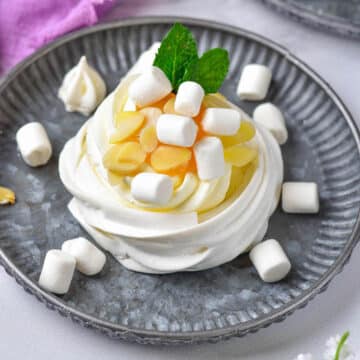 Mini pavlova with marshmallows and lemon curd on a grey plate.