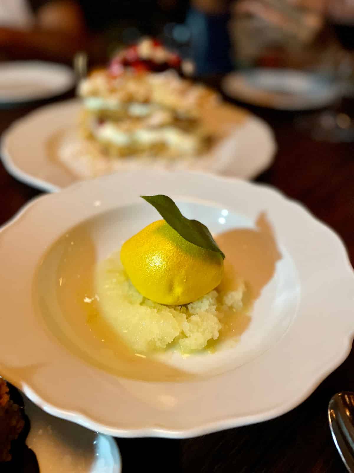 Lemon dessert over sorbet with a green leaf on a white plate.