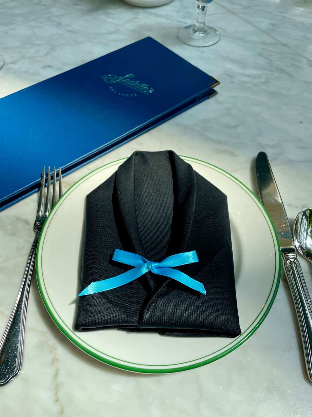 Napkin folded like a tuxedo on table with silverware.