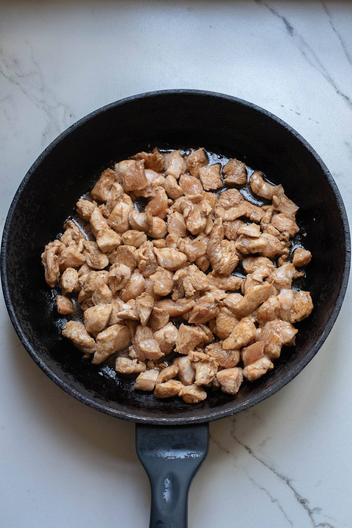 Chunks of chicken cooking in a cast iron pan.