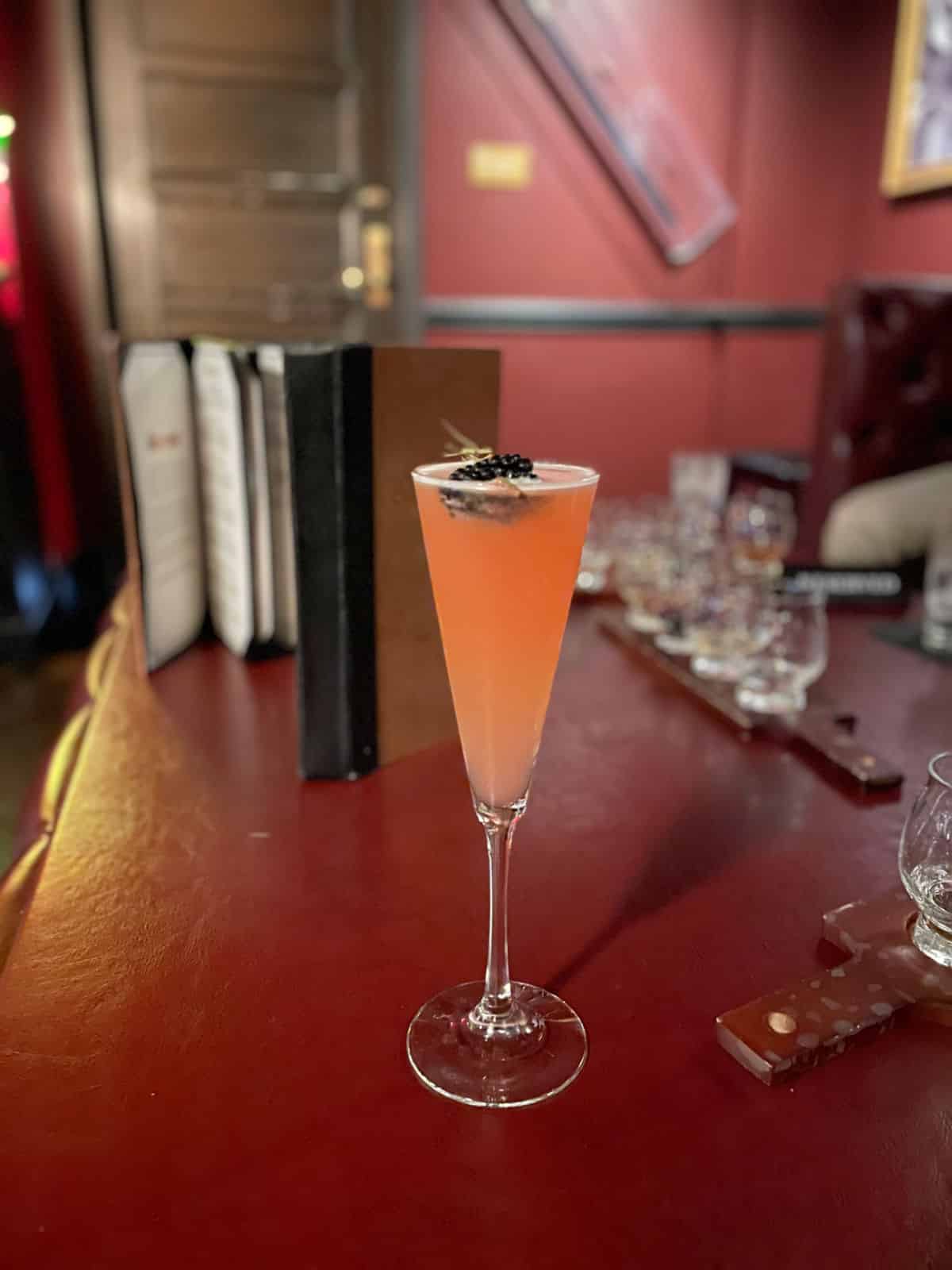 Peach cocktail with a blackberry on a red table.