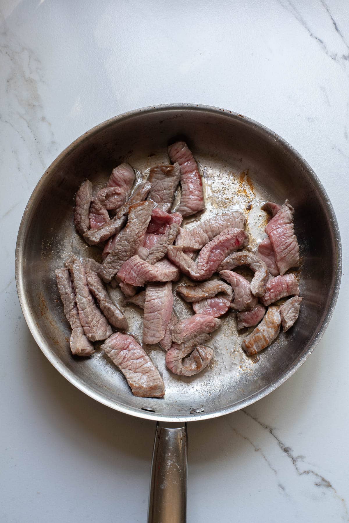 Sliced steak in stainless pan.