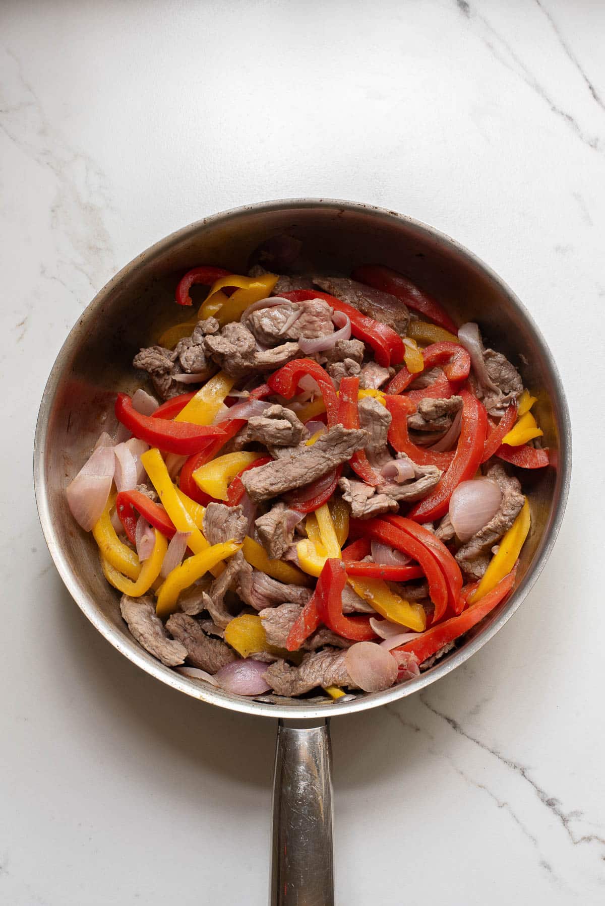 Sliced steak and pepper and onions in a stainless pan.