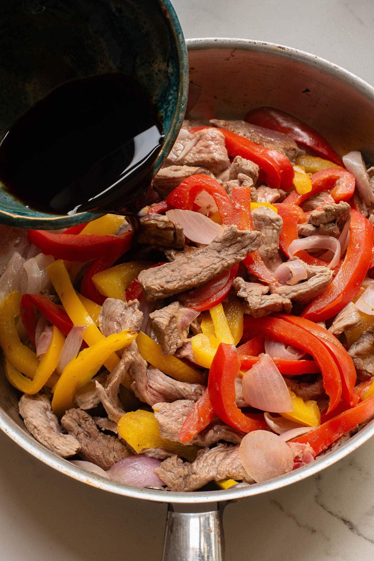 Steak, peppers, and onion, with sauce pouring over.