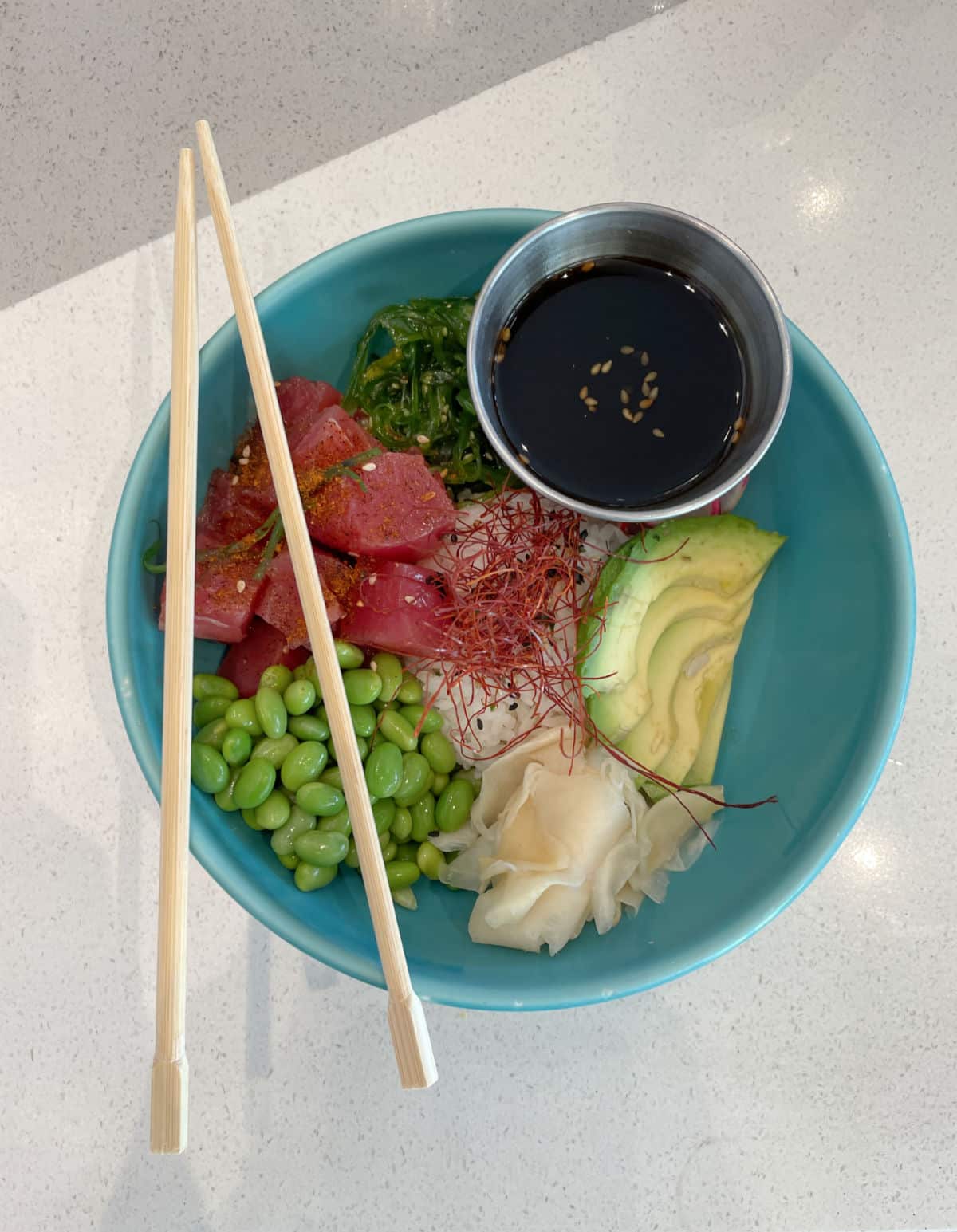 Tuna poke in a blue bowl with chopsticks.