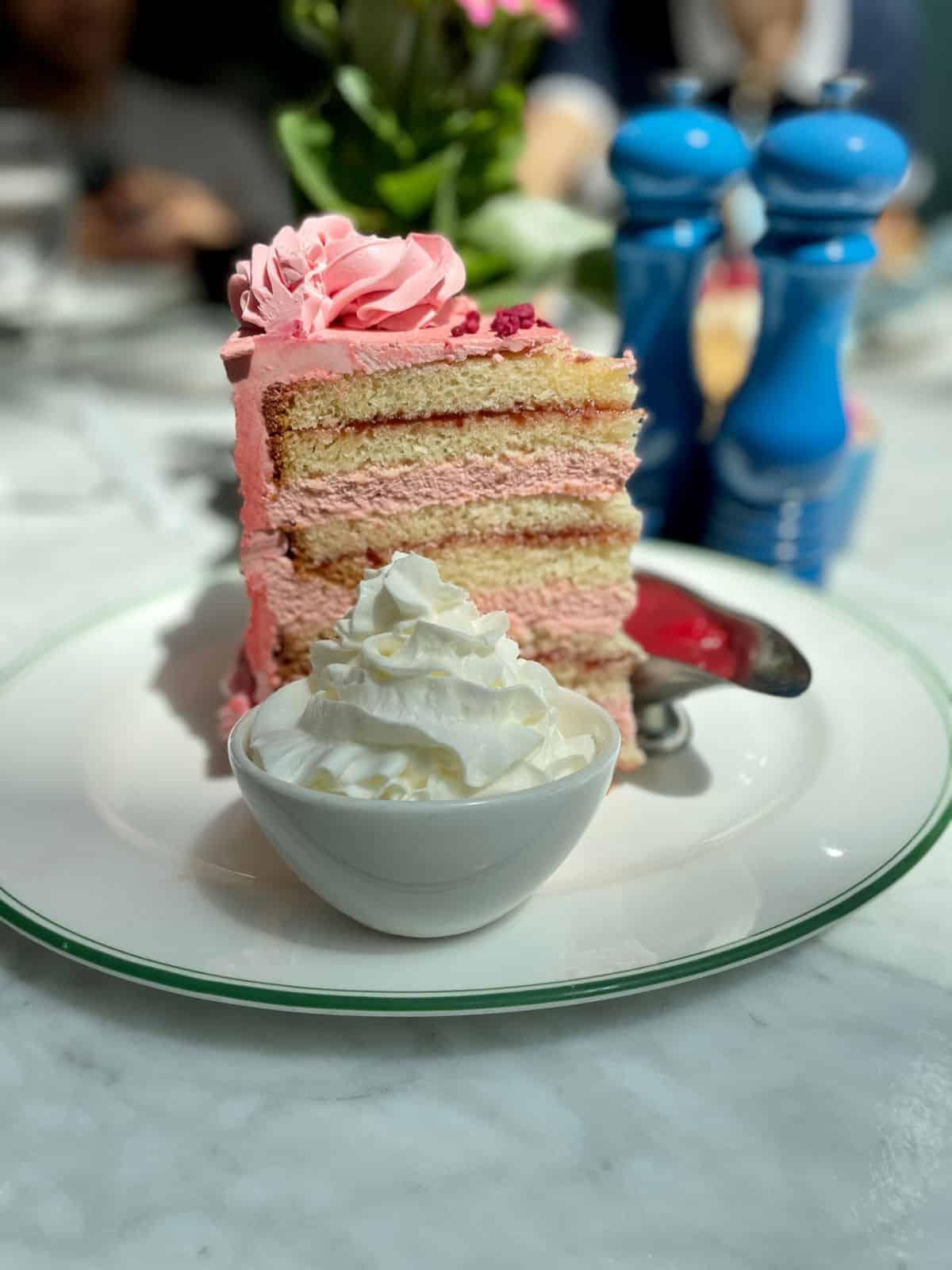 Tall cake slice with pin icing and whipped cream in a bowl.