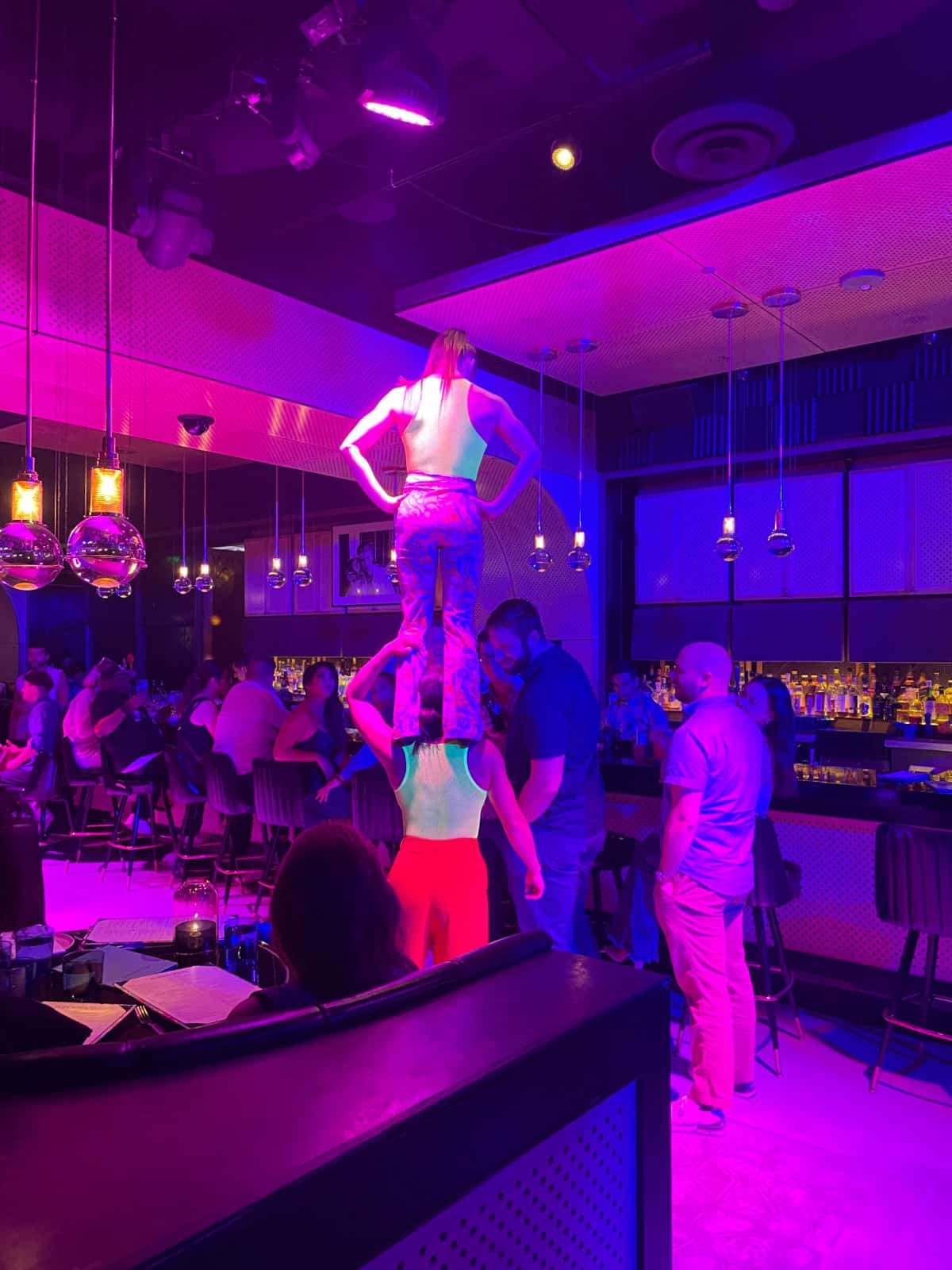 Woman standing on another woman's shoulders in a bar.