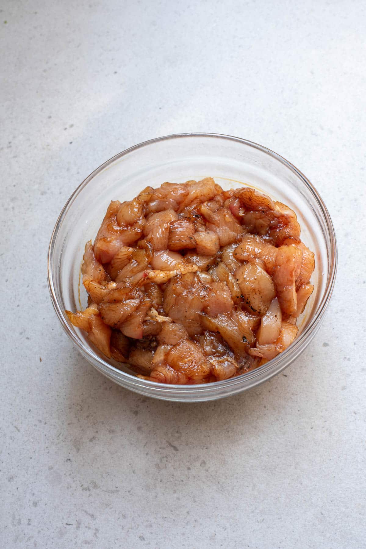 Chicken in marinade in glass bowl.