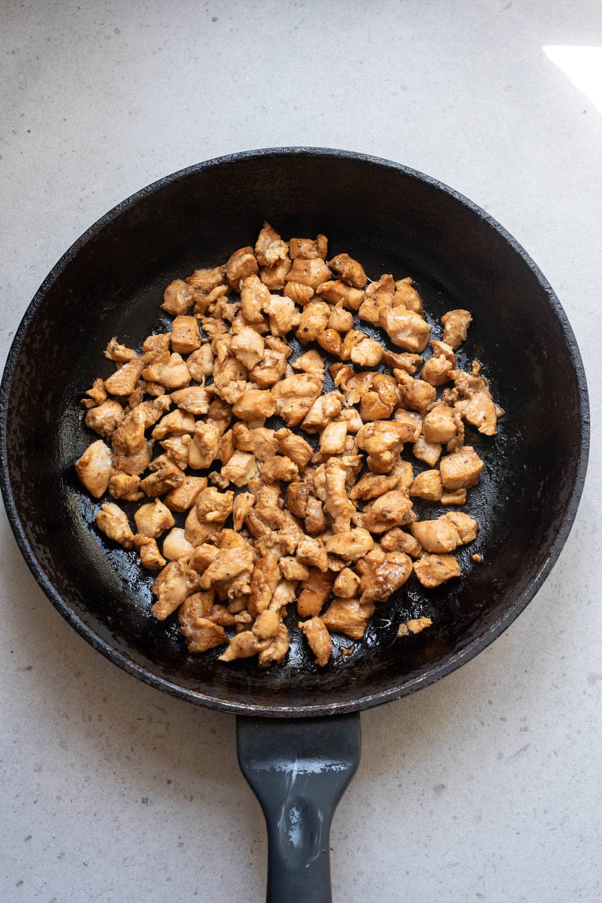 Cooked pieces of cubed chicken in a black skillet.