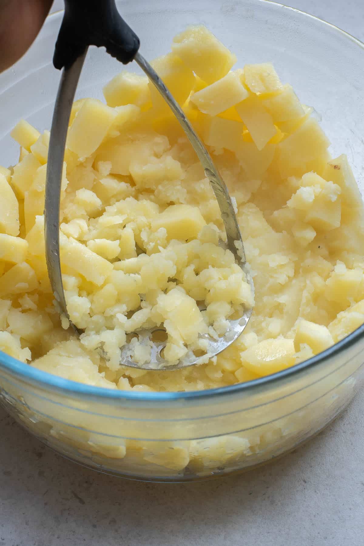 Potatoes being mashed in a glass bowl.