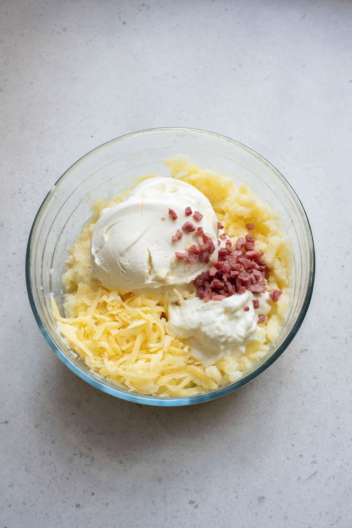 Potatoes, cream cheese, sour cream, bacon, and cheese in a glass bowl.