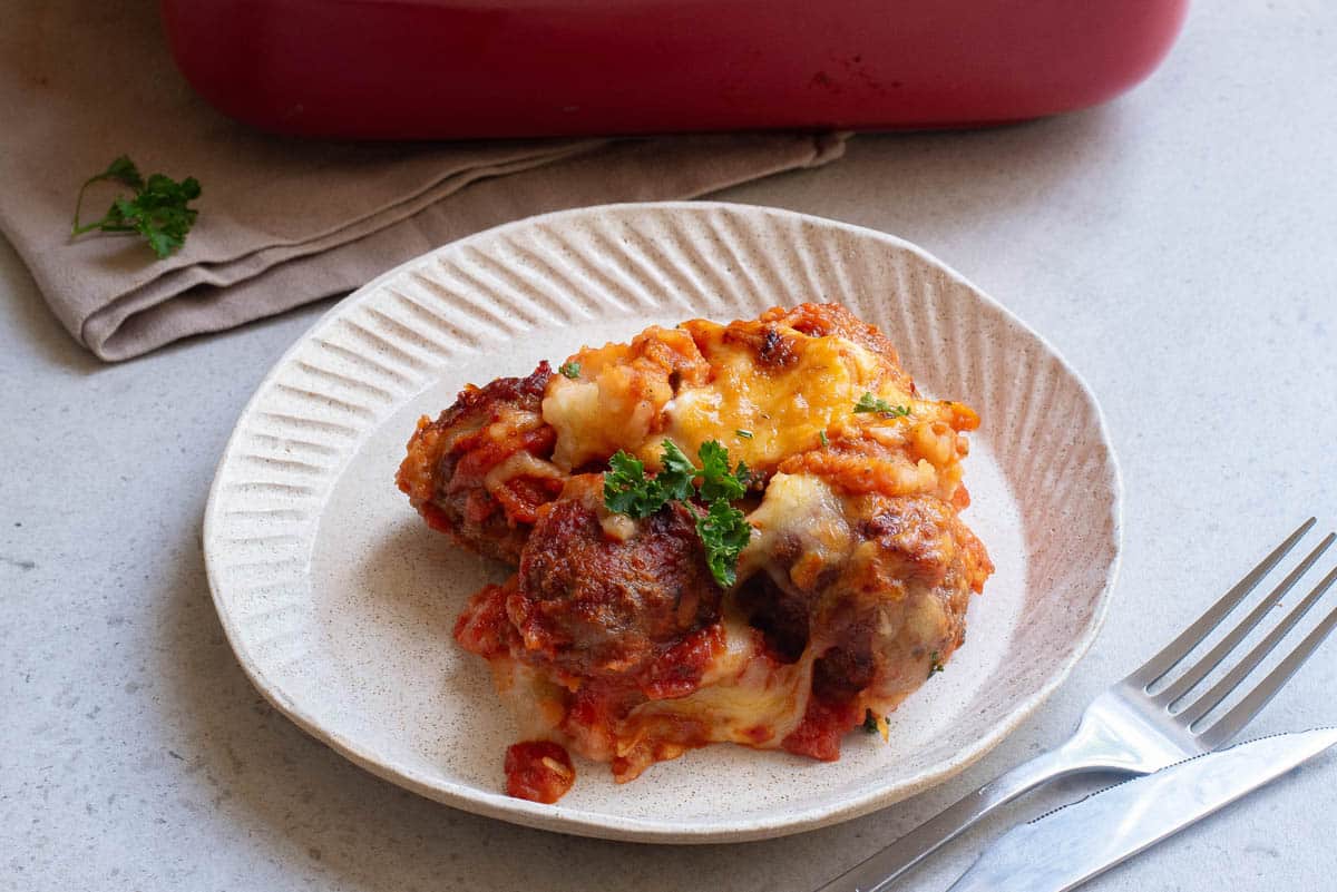 Meatballs, cheese, and potato casserole on white plate with silverware.