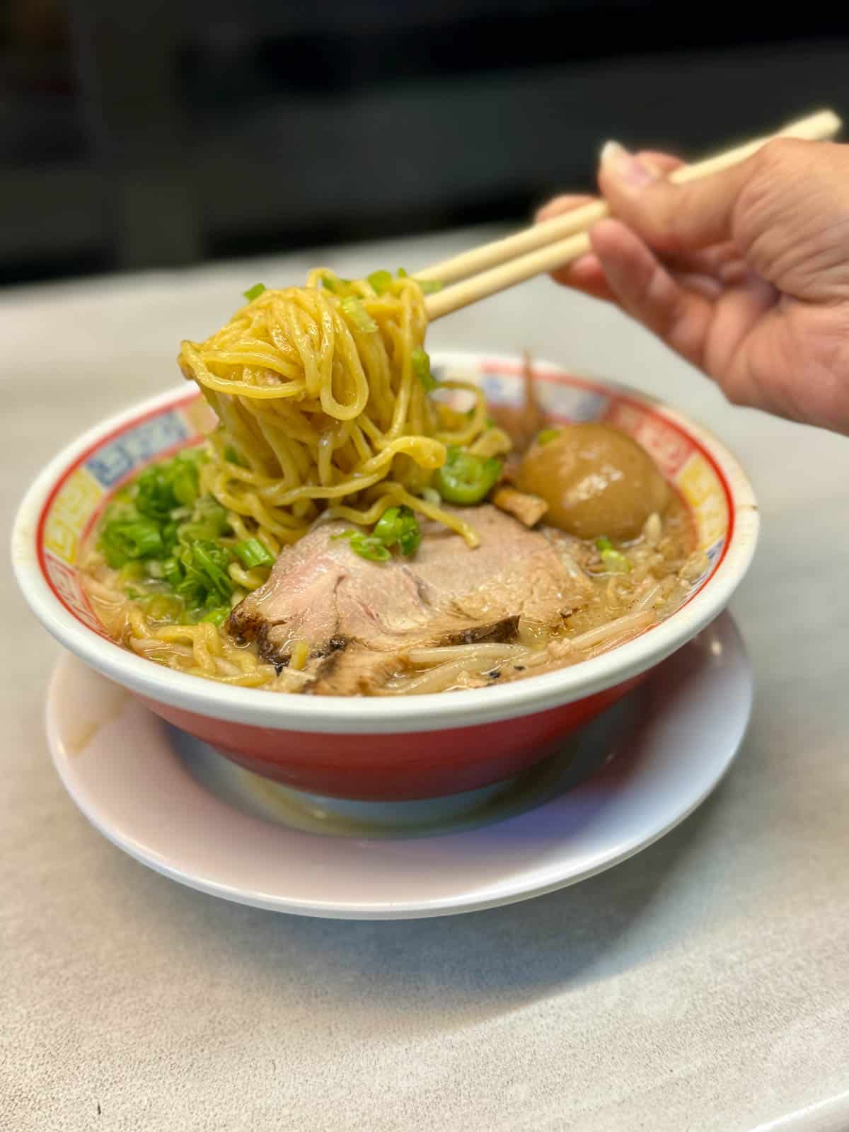 Bowl of ramen with hand holding noodles with chopsticks.