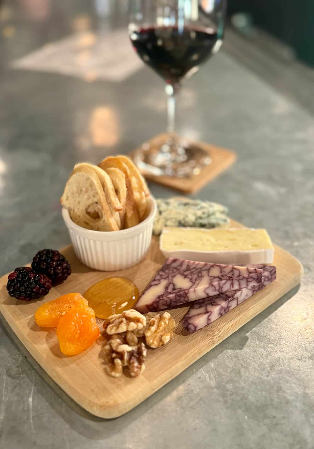 Cheese platter with dried fruit and honey and side of bread with glass of wine.